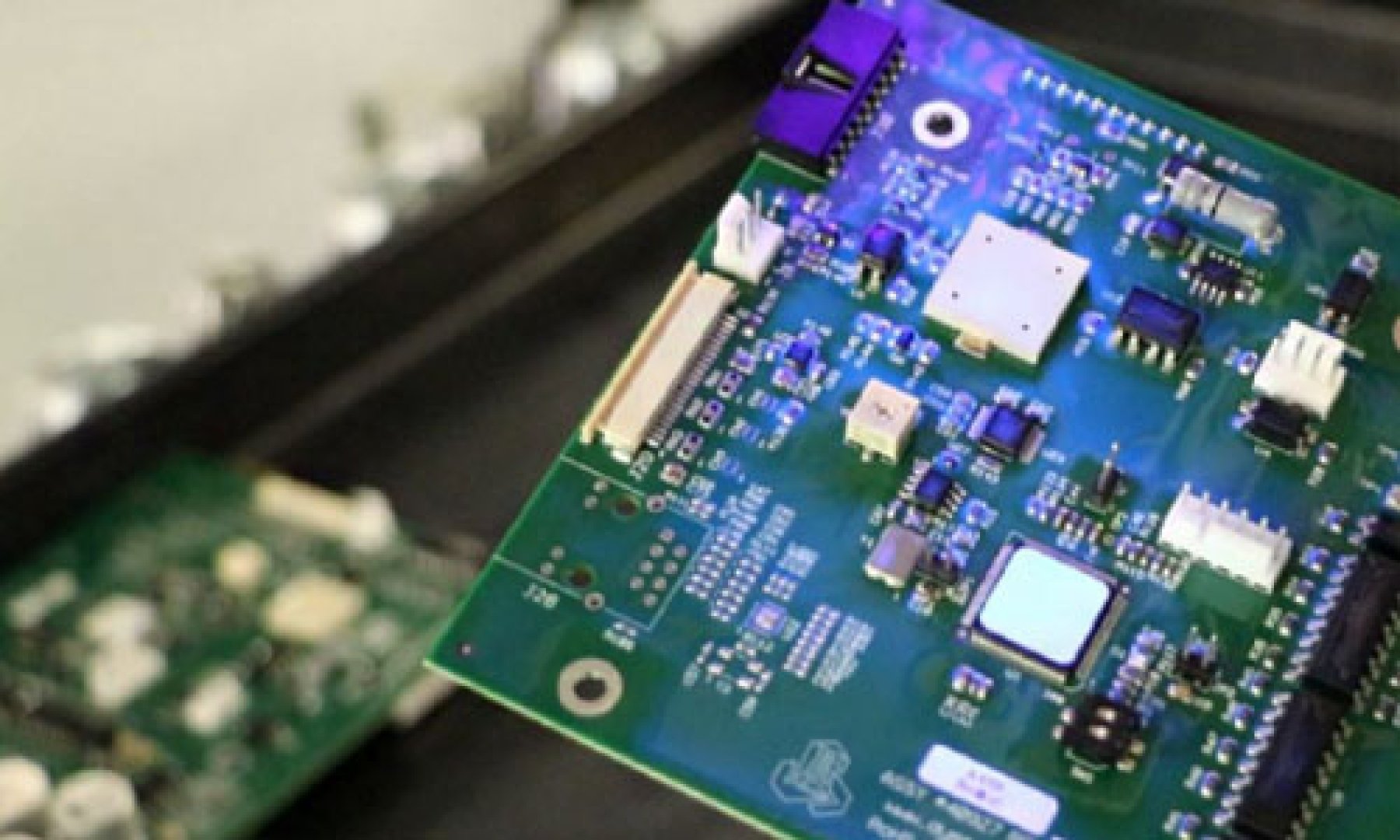 A printed circuit board with Dymax 9483 conformal coating fluoresces bright blue for quality inspection.